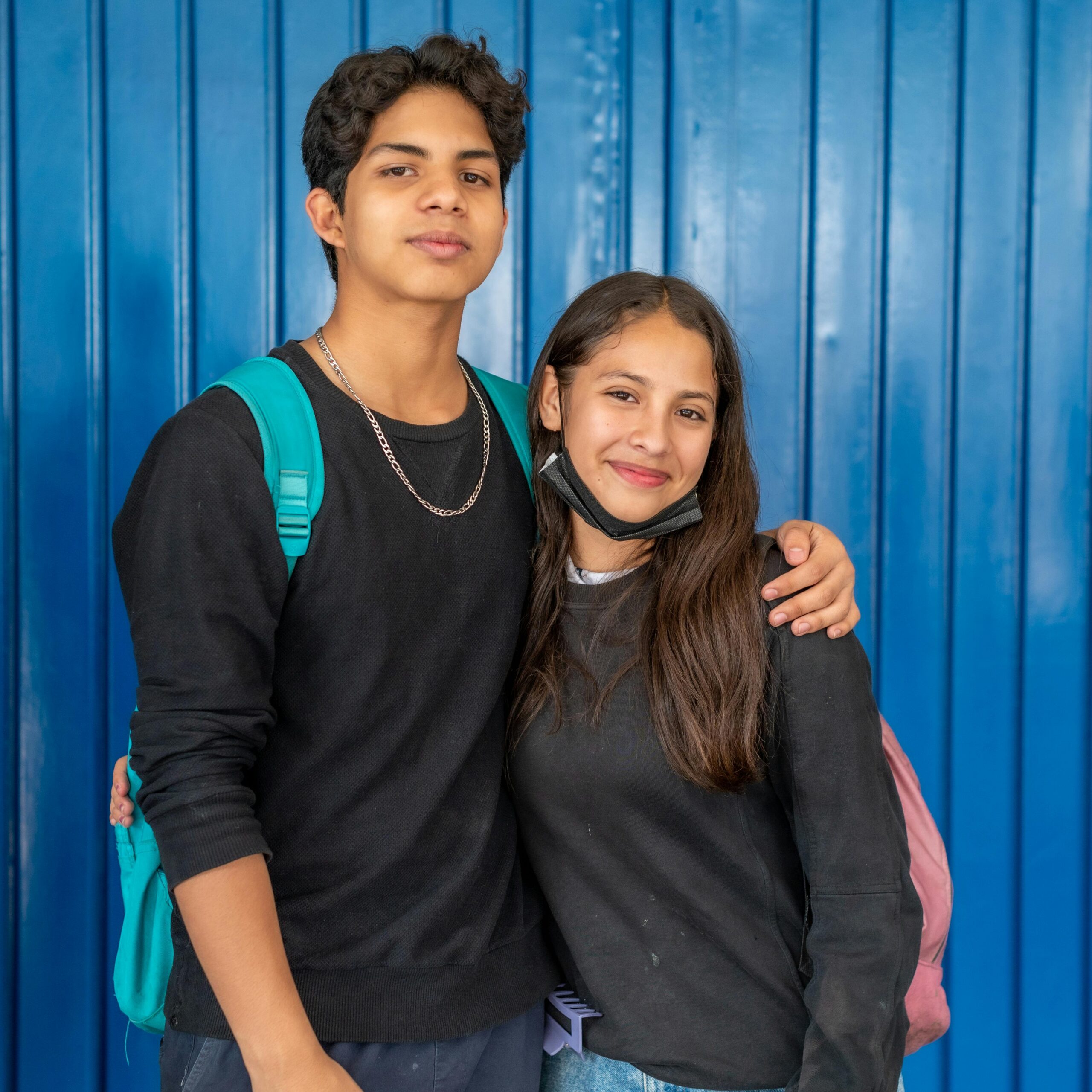 A cheerful young couple hugging in front of a vibrant blue background.